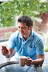 Man holding a cup of coffee and listening to music on a mobile phone
