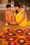 Woman and her son decorating rangoli with oil lamps on Diwali