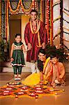 Family decorating rangoli with oil lamps on Diwali