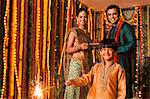 Boy burning fire crackers with his parents in the background on Diwali