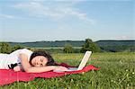 Girl with laptop sleeping in meadow