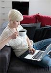 Young woman with cup using laptop on couch