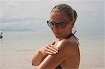 Woman on beach applying suntan lotion, Thailand