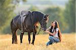 Young woman kneeling beside a Friesian horse in a cut cornfield, Bavaria, Germany