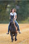 Portrait of young woman riding a Friesian horse in a cut cornfield, Bavaria, Germany