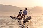 Intha 'leg rowing' fishermen at sunset on Inle Lake who row traditional wooden boats using their leg and fish using nets stretched over conical bamboo frames, Inle Lake, Myanmar (Burma), Southeast Asia