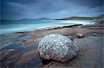 Large erratic boulder on the rocky coastline at Scarista with a view over the sand towards the hills of Taransay, Scarista, Isle of Harris, Outer Hebrides, Scotland, United Kingdom, Europe