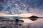 Winter sunrise on the Aln Estuary with a single boat moored on the mud flats, looking towards Church Hill reflecting in the calm water, Alnmouth, near Alnwick, Northumberland, England, United Kingdom, Europe