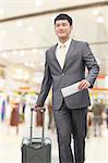 Young business man walking with suitcase and holding flight ticket in airport