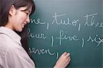 Young woman student writing English numbers on blackboard