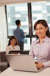 Businesswoman working on her laptop, coworkers on the background