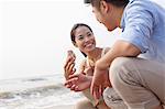 Young couple looking at seashell at the waters edge, China