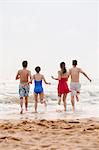 Four friends running into the water on a sandy beach