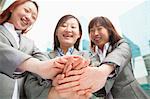 Three young businesswomen putting hands together, low angle view