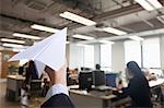 Hand holding paper airplane in office