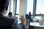 Businessman with feet up drinking coffee and text messaging