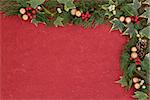 Christmas floral border with gold bauble decorations, holly, mistletoe, ivy, fir leaf sprigs over red mottled  background.