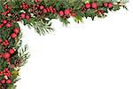 Christmas and winter border with red baubles, natural holly, mistletoe, ivy, fir leaf sprigs and pinecones over white background.