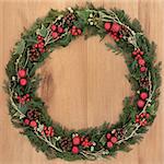 Christmas wreath with red bauble decorations, holly, mistletoe, ivy, pine cones and cedar and gold leaf sprigs over oak background.
