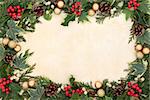 Christmas border of natural holly, ivy, mistletoe and gold bauble decorations over old parchment background.