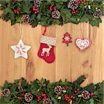 Christmas eve symbols of red stocking, tree, star and heart, with holly, ivy and mistletoe over oak background.