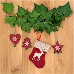 Christmas eve symbols of red stocking, tree, star and heart with ivy leaf sprigs over oak background.
