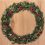 Christmas wreath with holly, mistletoe, ivy, pinecones and cedar leaf sprigs over golden oak background.