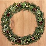 Natural christmas wreath with mistletoe, ivy, pinecones and cedar leaf sprigs over golden oak background.