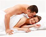 Young naked man leaning over young cheerful woman laying in bed