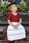 Portrait of a beautiful young blond Bavarian girl in a dirndl sitting quietly on a garden bench looking in a daydream