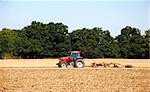 Red tractor and disc harrow breaking up the soil after harvest in a farm field - Kent, England