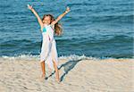 Happy summer jump by the sea on the beach - little girl expressing joy