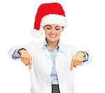 Smiling doctor woman in santa hat pointing down on copy space