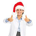 Smiling doctor woman in santa hat showing thumbs up