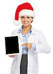 Happy doctor woman in santa hat pointing on tablet pc blank screen