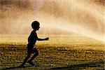 little boy running under the fountain sprays at the park