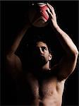 one caucasian sexy topless man portrait tossing a rugby ball on studio black background
