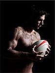 one caucasian sexy topless man portrait holding a rugby ball on studio black background a rugby ball on studio black background
