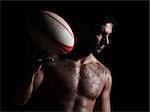 one caucasian sexy topless man portrait tossing a rugby ball on studio black background