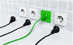 ecological green plug is connected to a green socket placed on the wall and three other traditional plugs are disconnected and lie on the ground