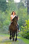 Portrait of a young woman riding a Friesian horse on a forest pathway, Bavaria, Germany