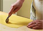 Close-up of elderly Italian woman making pasta by hand in kitchen, cutting pasta dough with rotary tool, Ontario, Canada