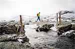 Hiker crossing small bridge over mountain stream, Norway, Europe