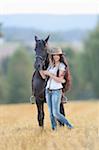 Young Woman Standing beside Friesian Horse in threshed Cornfield, Bavaria, Germany