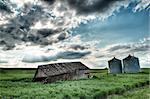 Barn in a green field next to silos with sun rays shining through the clouds
