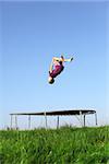 Young boy doing a backflip on a trampoline on green meadow