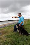 A man pointing out to sea with his dog by his side