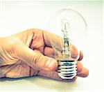 A hand holding a lightbulb against white background
