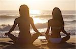 Two sexy young women or girls wearing bikinis sitting cross legged on a deserted tropical beach at sunset or sunrise