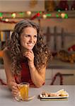 Happy young woman drinking ginger tea in christmas decorated kitchen